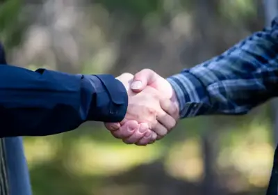 Kaksi ihmistä sinisissä paidoissa kättelevät metsässä