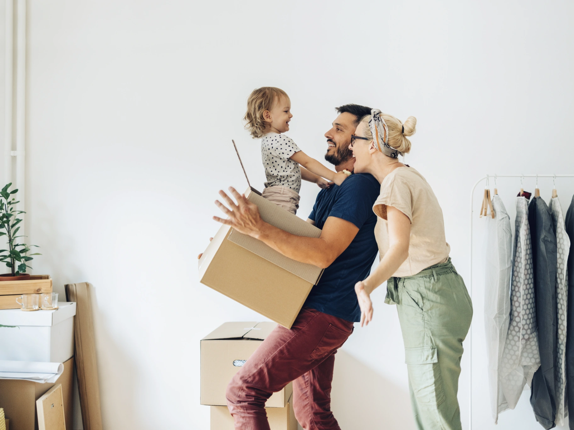 Happy family with one child having fun while carrying and unpacking boxes in new home on moving day