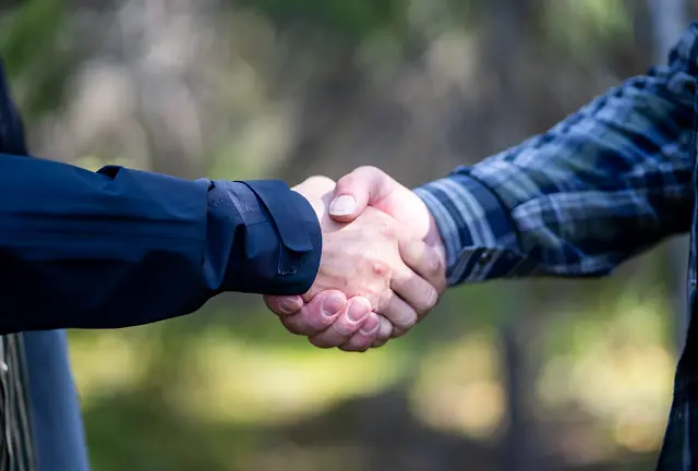 Kaksi ihmistä sinisissä paidoissa kättelevät metsässä
